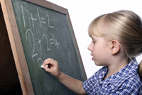 child writing on chalboard; young girl doing writing math problems on a chalkboard